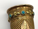 a gold vase with turquoise stones in it on a table