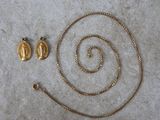 two gold necklaces and a pair of earrings laying on a white surface