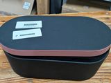 une boîte noire avec un couvercle rose posée sur une table en bois
