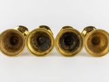 four brass candlesticks are lined up on a white surface