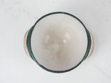 a white bowl with a green rim on a white surface