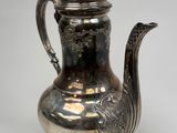 an antique silver tea pot with a bird handle on a stand