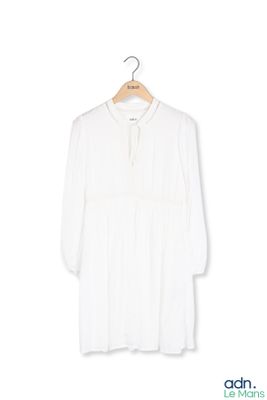 La chemise blanche est suspendue à un cintre accroché à un mur blanc.