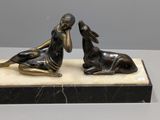 deux statues en bronze représentant une femme et un chien, posées sur un socle en marbre