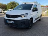 La camionnette blanche est garée sur le parking, à côté d'une clôture.