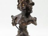 un buste en bronze représentant une femme tenant un oiseau, posé sur un socle en bois