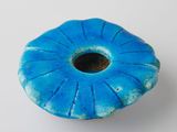 un vase bleu troué posé sur une surface blanche