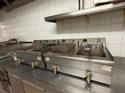 Plusieurs friteuses sont alignées sur un plan de travail dans une cuisine professionnelle.