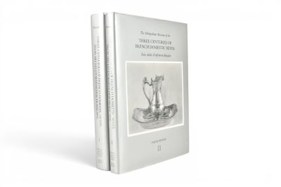 Le livre repose sur une surface blanche sur laquelle est posé un vase argenté.