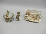 trois figurines en porcelaine et une boîte posées sur une surface blanche