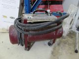 a red air compressor sitting on the floor next to a pile of tools