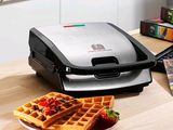 a waffle maker sitting on a table with a plate of waffles next to it