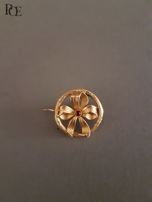 une image représentant une broche en forme de fleur en or, ornée d'une pierre rouge au centre