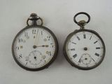 two antique pocket watches sitting side by side on a white surface