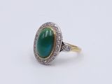 a close up of a ring with a green stone surrounded by diamonds