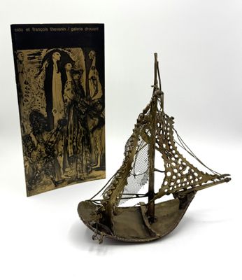 une maquette ancienne en laiton représentant un voilier, avec un livre en arrière-plan