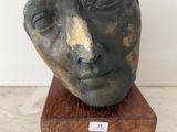 une photo d'une sculpture représentant le visage d'un homme, posée sur un socle en bois