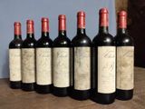 six bottles of red wine lined up on a wooden table