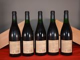 six bottles of wine are lined up on a red cloth