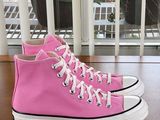 pink converses on a wooden table near a window with a potted plant in the background