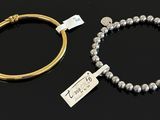 two silver bracelets and a gold bang with a tag