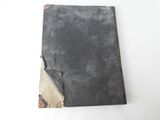 an old book with a black cover sitting on top of a white table