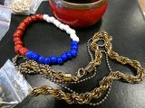 a red, white and blue bracelet and a gold chain on a table
