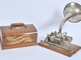 un gramophone argenté posé sur un socle en bois, à côté d'une boîte en bois