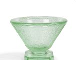 un bol en verre vert posé sur un socle, sur une surface blanche
