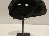 sculpture of a black mask on a black stand on a white surface