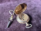 une montre de poche en argent et une clé posées sur un tissu violet