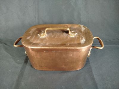 une vieille cocotte de couleur cuivrée avec des poignées, sur fond noir