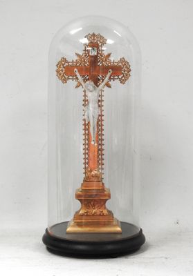 une croix richement décorée, placée sous un dôme en verre et reposant sur un socle en bois