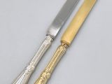 a pair of silver and gold plated knives on a white surface