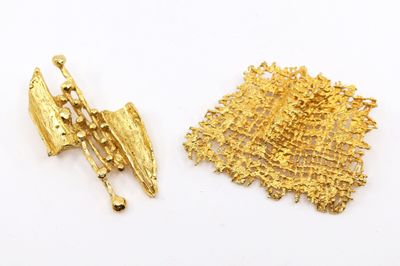 un gros plan sur deux broches en or posées sur une surface blanche