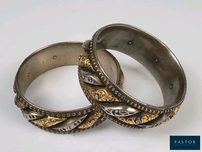 pair of silver and gold bangles on a white surface with a blue background