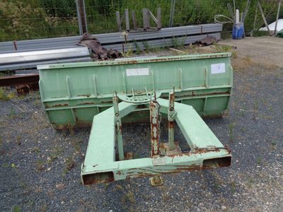 a green dumpster sitting in the gravel next to a pile of metal