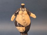figurine représentant un homme corpulent, posée sur un socle noir, sur fond bleu