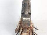 a wooden mask with feathers on it on a white surface