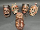 six carved wooden masks are lined up on a black surface
