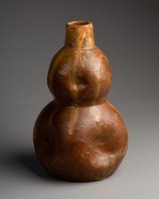 un vase marron posé sur une table près d'un mur gris
