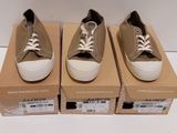 trois paires de chaussures sont posées sur des cartons, sur une surface blanche