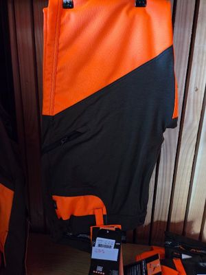 an orange and black jacket hanging on a wooden wall next to a pair of shoes