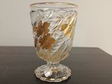un vase en verre orné de feuilles dorées, posé sur une table