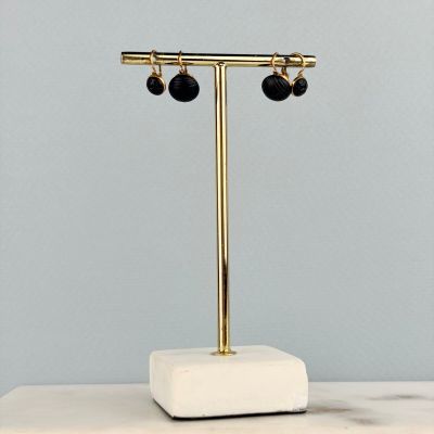 des boucles d'oreilles dorées et noires posées sur un socle en marbre, lui-même posé sur une table en marbre