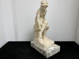 statue en marbre représentant un homme assis sur un rocher, posée sur un socle noir