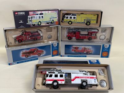 trois camions de pompiers miniatures dans leurs boîtes, posés sur une surface blanche