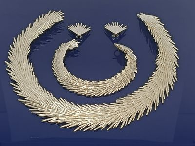 un ensemble composé d'un collier et de boucles d'oreilles en or, posé sur un fond bleu