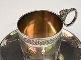 a silver cup and saucer sitting on a saucer