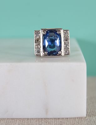 an image of a blue sapphire and diamond ring sitting on a white marble block